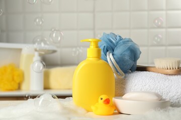 Baby cosmetic products, bath duck, brush and towel on white table against soap bubbles