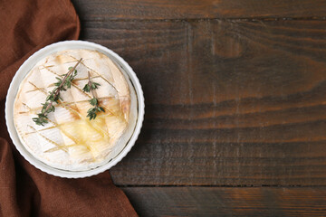 Tasty baked camembert and thyme in bowl on wooden table, top view. Space for text