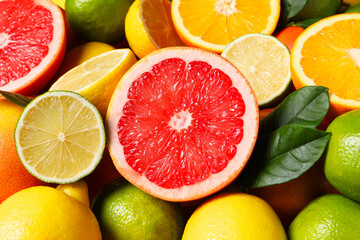 Different fresh citrus fruits and leaves as background, closeup