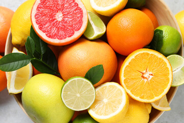 Different fresh citrus fruits and leaves in bowl on light table, top view