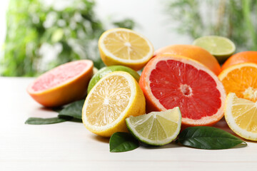 Different cut and whole citrus fruits on white wooden table, closeup