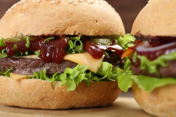 Delicious cheeseburgers with lettuce, pickle, ketchup and patty on wooden table, closeup