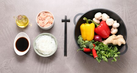 Wok, chopsticks and different products on grey textured table, flat lay