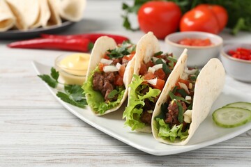 Delicious tacos with meat and vegetables on wooden table, closeup