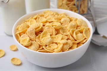 Tasty crispy corn flakes in bowl on white table, closeup. Breakfast cereal
