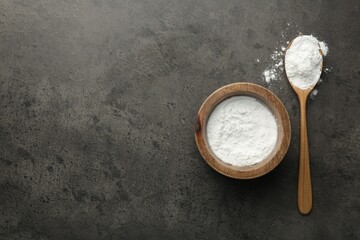 Baking powder in bowl and spoon on grey textured table, top view. Space for text