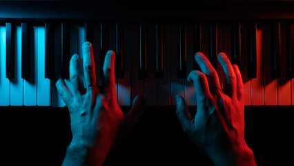 Close-up hands of a pianist playing a keyboard instrument (piano, grand or synth) in a red and blue...
