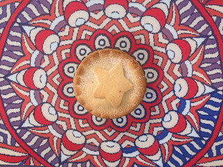 Fruit mince pie decorated with a star. Fabric Mandala background