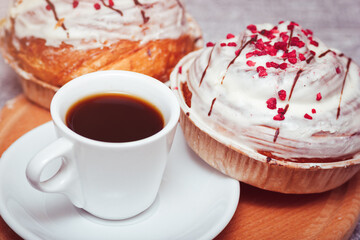 The cup of espresso coffee with cinnabon sweet buns. Tasty pastry with cream glaze and pink decoration.