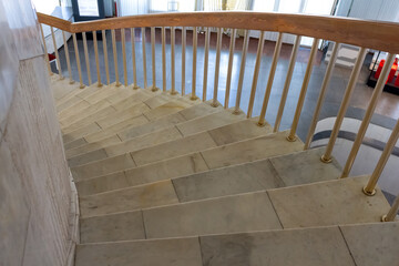 Close-up view of spiral staircase with marble steps and wooden railing inside of building. Soft focus. Copy space for your text. Architecture details theme.