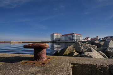 Obraz premium A CITY BY THE SEA - Old rusty bollard on the port quay and a holiday resort in the background