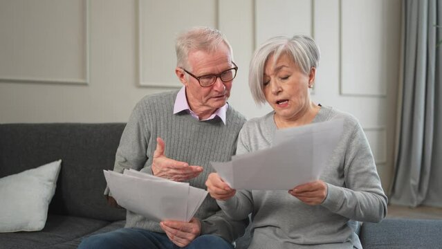 Sad tired disappointed middle aged senior couple sit with paper document. Unhappy older mature man woman reading paper bill managing bank finances calculating taxes planning loan debt pension payment