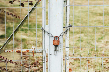Closed metal fence. Padlock background. Abandoned property. Gate closed with metal chain. Private property forbidden entry. Padlock hanging on chains.