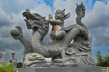 Obraz premium Little buddha riding on the dragon and waving to worshippers. Beautiful stone crafted statue in 500 statue Buddha temple in bintan Indonesia