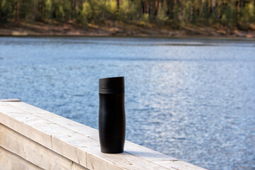 
Black thermos on wooden board with blue water background