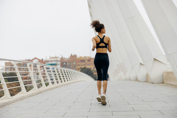 Back view of woman athlete is jogging on morning on modern building background. Healthy life concept