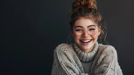 Foto op Canvas Against a comfortable dark background, a stylish young lady with a messy bun, wearing trendy glasses and a comfy oversized sweater, is seen laughing merrily © Stone Shoaib