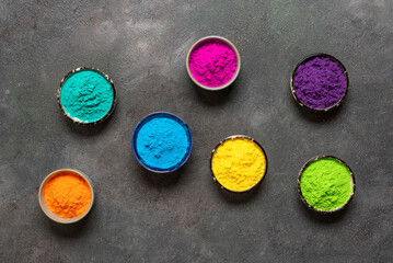 Obraz na płótnie Canvas Colorful Holi powders. Organic colors Gulal in bowl for Holi festival on dark background. Top view, flat lay, copy space.