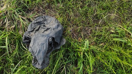 Black dirty plastic bag on the grass of park during sunny 