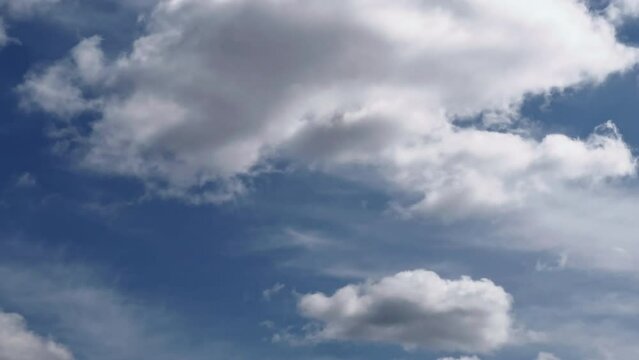Roughly swelling white cumulus clouds flowing in the blue sky. Cloudscape time-lapse footage.