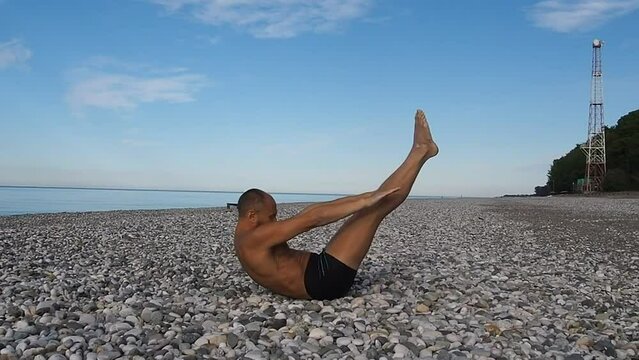 A man on the beach does yoga. Yoga asanas on the sea beach. Healthy lifestyle concept