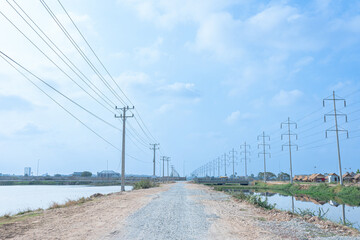 Electric power lines stretch across the vibrant landscape, traversing roads and fields under a blue sky, weaving through nature and industry, creating a dynamic visual of energy connectivity