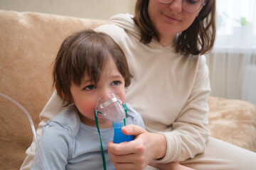 Inhalation for a sick asthmatic child to treat allergies. A mother woman with an inhaler helps her...