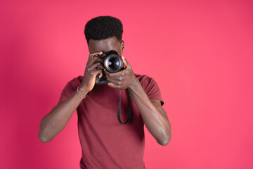 Young black man taking a photograph with a mirrorless camera, wearing a red t-shirt on a carmine red background with copy space.
