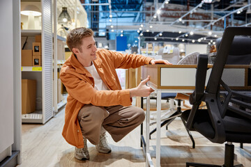 Young man choosing desk table for home office interior remodeling