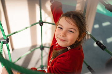 Close-up of a smiling child on a rope net at a park, embodying playful moments and happiness