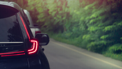 Rear side view of dark car with red light of brake. Driving speed on the aspahtl road with blurred...