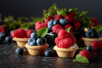 Small tartlets with fresh raspberries and blueberries on a black background.