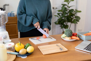 Obraz na płótnie Canvas Woman slicing veggies on a cutting board in the kitchen