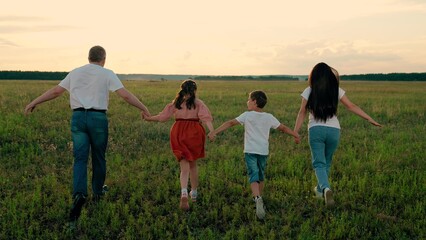 Happy family, Children with parents run across field. Children parents playfully enjoy time spent together on weekend on park. Happy children with father and mother spend time on grass field at sunset