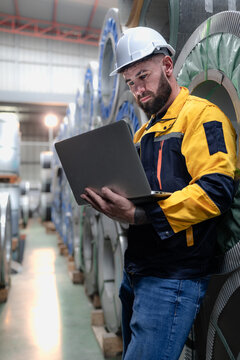 Industrial engineer in safety helmet uniform jacket working in heavy steel engineering factory. Technician manager worker inspector using laptop in metalwork product manufacturing facility workplace