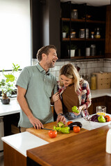 Smiling man and woman chopping fresh vegetables on a kitchen island, enjoying a healthy cooking activity together