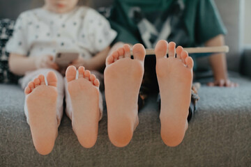 Big brother and little sister holding bare feet close up to camera . Blurred face on background 