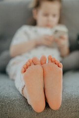 little girl holding bare feet close up to camera and reading book . Blurred face on background 