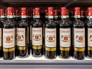 Fototapeta premium Italy - March 02, 2024: Chianti wine in bottles displayed on shelf for sale in wine shop. Chianti is typical wine from Tuscany, Italy