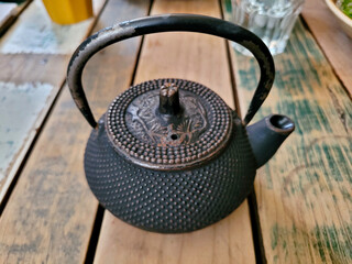 An antique cast iron teapot with intricate designs, presented on a rustic wooden surface