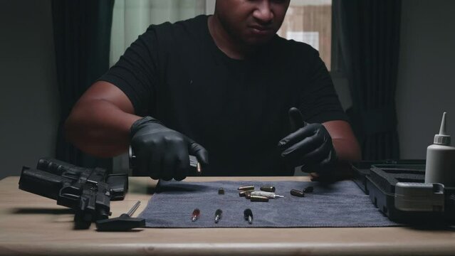 Slow motion image of a man sitting alone in a room. He unloads an ammunition 9 mm. magazine full of bullets before cleaning his weapon.assembling the gun. military ammunition. weapon care.