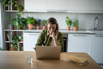 Thoughtful serious woman freelancer working from home look at screen of laptop. Busy accountant...