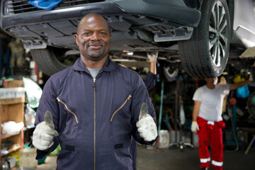 mechanic smiling and thumbs up pose in automobile repair shop