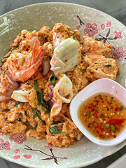 Omelette with pork and seafood on rice and sauce on white ceramic plate and spoon and fork.