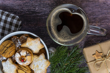 Weiße Porzellanschale mit Weihnachtskeksen auf dunklem Holzhintergrund, Kaffee in herzförmiger Glastasse, Draufsicht, horizontal