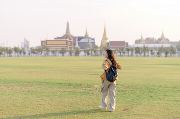 Traveler asian woman in her 30s, backpack slung over her shoulder, explores Wat Pra Kaew with...