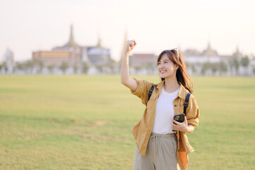 Traveler asian woman in her 30s navigates the bustling grounds of Wat Pra Kaew. Technology helps...
