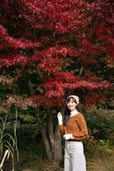 Asian woman in a fashionable sweater revels in the beauty of fall. A pretty and cheerful portrait amid nature's vibrant colors.