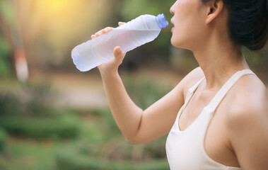 Female runner. Fit Asian young woman with white sportswear drinking water after running and...