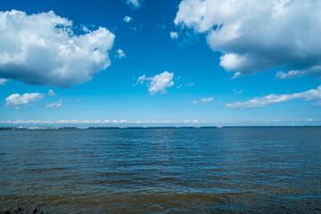 View from the shore to the sea bay in summer. The sky above the water with white clouds.